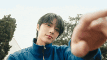 a young man in a blue jacket is taking a selfie with his finger .