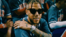a man wearing sunglasses and a watch is sitting in a crowd of people