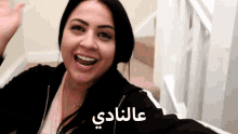 a woman in a black jacket is smiling in front of stairs with arabic writing on the bottom