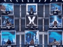 a group of people sitting in front of a wall with the letter x on it .