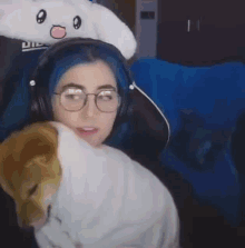 a woman with blue hair and glasses is wearing headphones and a bunny hat while holding a stuffed animal .