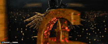 a statue of a man with wings and a spear is surrounded by the letter g