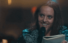 a man with long hair is holding a book and smiling with the words " i mean ... why ? " behind him