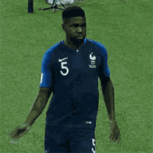 a man in a blue jersey with the number 5 on it is running on a soccer field .