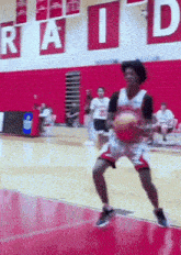 a basketball player is dribbling the ball in front of a sign that says raid