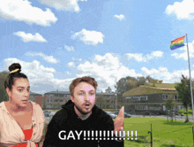 a man and a woman are standing in front of a building with a rainbow flag in the background and the man says gay !!!