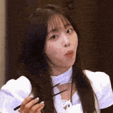 a young woman in a white dress is holding chopsticks in her hand .