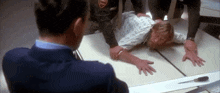 a man in a suit and tie is looking at a man laying on a table .