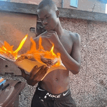 a shirtless man wearing nike shorts holds a burning book