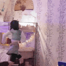 a girl dancing in a bedroom with a fan hanging on the wall