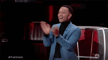a man in a blue suit and black turtleneck is applauding on a tv show called the voice