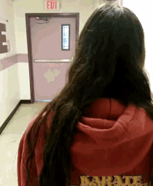 a woman in a red karate sweatshirt stands in front of a pink exit sign