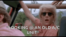 a woman wearing sunglasses is sitting in a car with her arm outstretched .