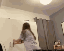 a woman in a purple shirt is opening a white cabinet