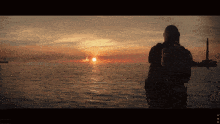 a man stands in front of a large body of water watching the sun set