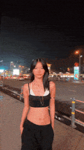 a woman in a black crop top and black pants is standing on a sidewalk at night .