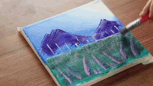 a person is painting a landscape with mountains and flowers