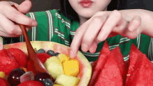 a woman is eating watermelon with a wooden spoon and a bowl of fruit .