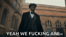 a man in a suit and bow tie is standing in front of a building and says yeah we fucking are .
