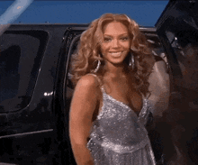 a woman in a silver dress is smiling while getting out of a limousine .