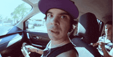 a man wearing a purple hat and a black tank top is driving a car
