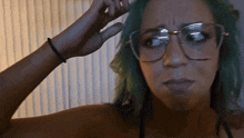 a woman with green hair and glasses has her finger on her forehead