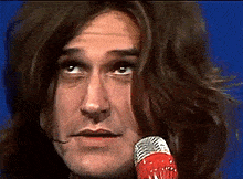 a man with long hair is singing into a microphone .