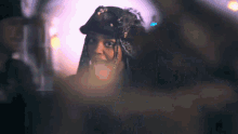 a woman with dreadlocks wearing a hat looks at the camera