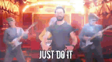 a man in a black shirt is standing in front of a group of people playing guitars and singing the words just do it