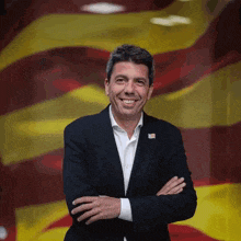 a man in a suit is smiling with his arms crossed in front of an american flag
