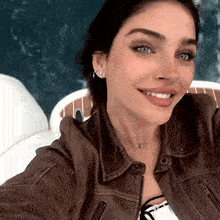 a woman wearing a brown leather jacket and earrings smiles for the camera