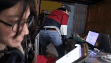 a woman wearing glasses looks at a man standing in front of a laptop computer
