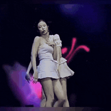 two women are dancing on a stage with purple lights in the background .
