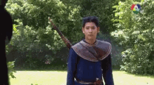 a man in a blue shirt is holding a bow and arrow in a park .