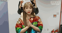 a woman in a colorful jacket is making a heart with her hands .