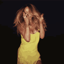 a woman in a yellow dress covers her face with her hands
