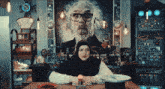 a woman in a hijab sits in front of a painting of einstein