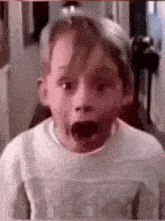 a young boy with his mouth open is wearing a white sweater .