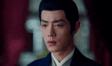 a close up of a man 's face with a red curtain in the background and a black jacket .