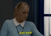 a woman in a blue sweater is saying " just wait "