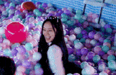 a girl in a cat ear headband is playing in a ball pit filled with colorful balls