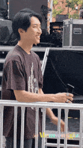 a man in a brown shirt is smiling and holding a cell phone in his hand