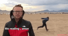 a man wearing glasses and a red jacket is standing in the middle of a desert with a woman running in the background .