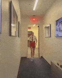 a person walking down a hallway with a red exit sign on the wall