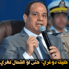 a man in a suit and tie is holding a microphone with arabic writing behind him