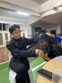 a man in a black jacket is covering another man 's face with a black veil