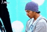 a man wearing a purple beanie and a gray hoodie is standing in front of a blue background .