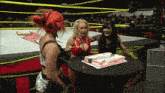three women in a wrestling ring with one holding a cake
