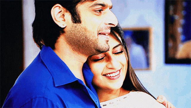 a man in a blue shirt is hugging a smiling woman