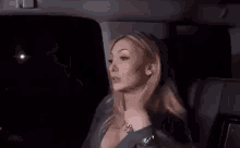 a woman is sitting in the back seat of a car with her hand on her face .